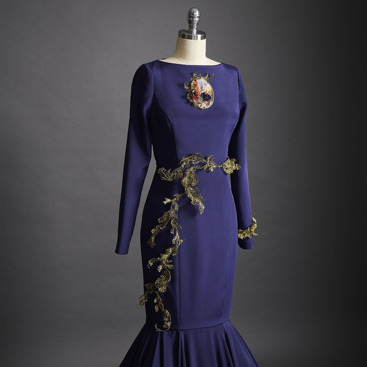 A navy blue crepe de chine dress featuring a sweeping fishtail train. The embroidery, a combination of golden French lace and wire, delicately wraps around the waistline of the dress. - DELPHINE GENIN